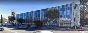Angled street view of a multi-story modern medical office building with blue-tinted glass panels and street parking.
